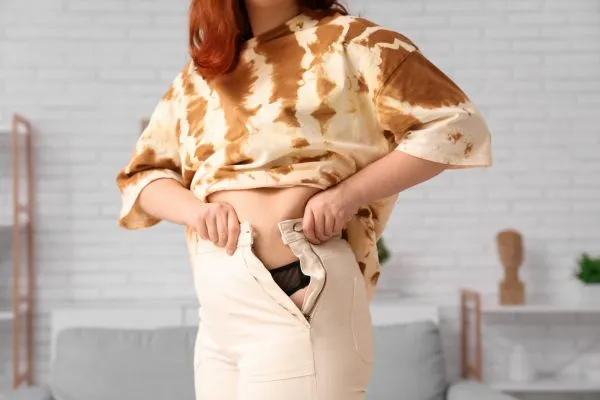 Image of woman trying to do her trousers up after pregnancy weight gain Hall Green
