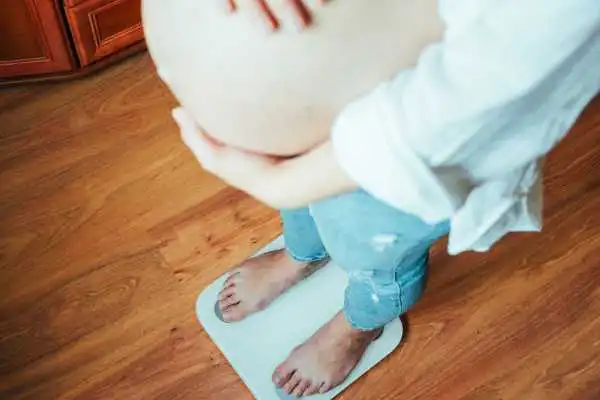 Image of woman weighing herself and experiencing weight gain through pregnancy Hall Green